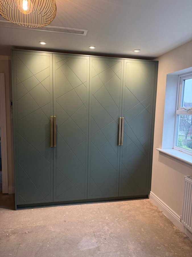 Sage green wardrobes with diagonal panelled doors and long brass handles